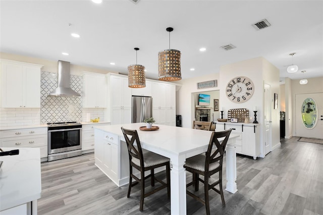 kitchen with appliances with stainless steel finishes, white cabinetry, hanging light fixtures, and wall chimney exhaust hood