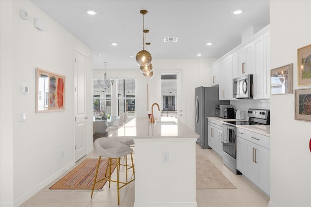 kitchen featuring appliances with stainless steel finishes, sink, decorative light fixtures, white cabinetry, and an island with sink