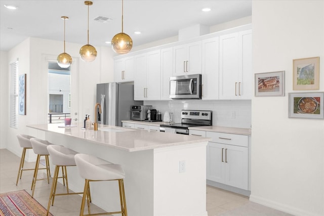 kitchen featuring white cabinetry, a kitchen island with sink, decorative light fixtures, and appliances with stainless steel finishes