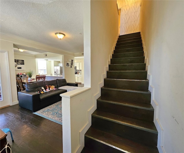 stairway with wood-type flooring, a textured ceiling, and ornamental molding