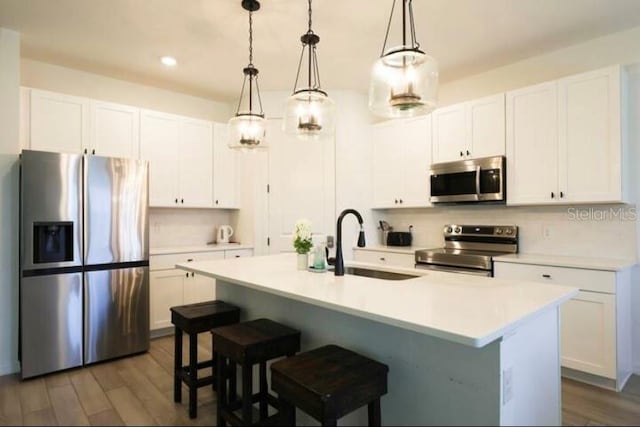 kitchen with pendant lighting, a kitchen island with sink, dark wood-type flooring, and appliances with stainless steel finishes