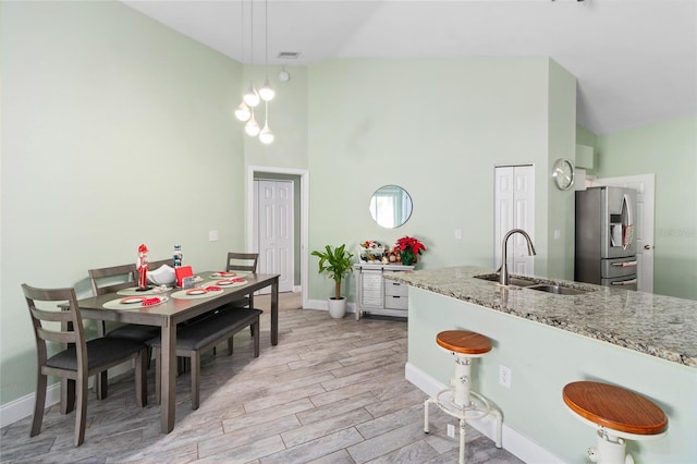 kitchen with pendant lighting, sink, stainless steel refrigerator with ice dispenser, light hardwood / wood-style flooring, and light stone counters