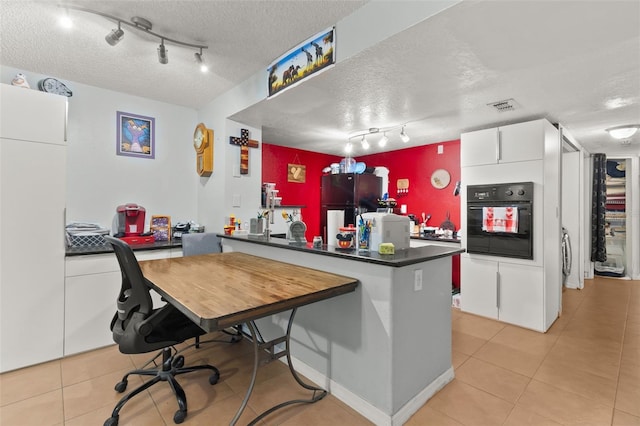 kitchen featuring refrigerator, rail lighting, a textured ceiling, black oven, and kitchen peninsula