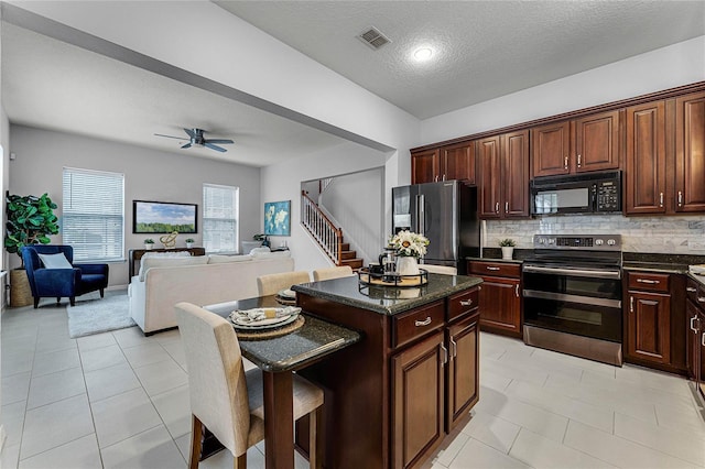 kitchen with backsplash, a textured ceiling, stainless steel appliances, ceiling fan, and a kitchen island