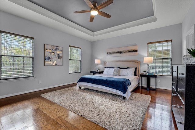 bedroom with ceiling fan, dark wood-type flooring, a tray ceiling, and multiple windows