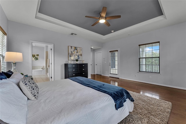 bedroom with hardwood / wood-style floors, a tray ceiling, ensuite bath, and ceiling fan