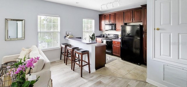 kitchen with rail lighting, light hardwood / wood-style flooring, kitchen peninsula, a breakfast bar, and black appliances