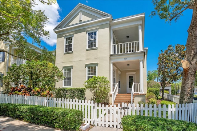 greek revival inspired property featuring stucco siding, covered porch, a fenced front yard, and a balcony