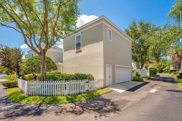 view of side of home featuring a fenced front yard, driveway, stucco siding, and an attached garage