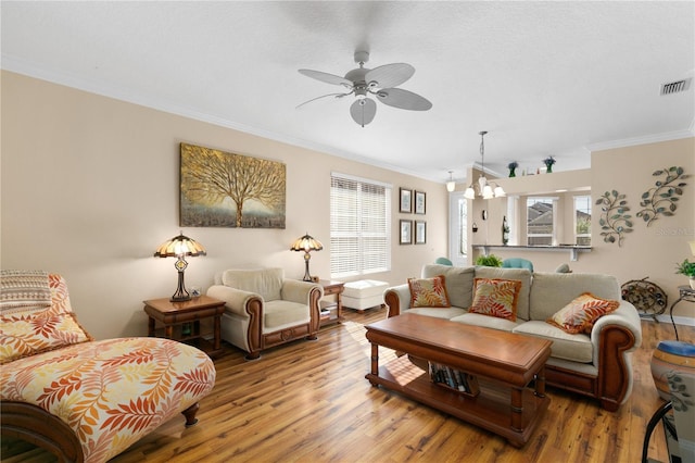 living room with light wood-style floors, visible vents, crown molding, and ceiling fan with notable chandelier