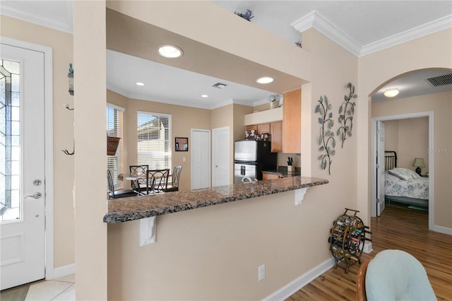 kitchen with a breakfast bar, freestanding refrigerator, ornamental molding, and arched walkways