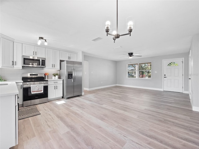 kitchen featuring light wood-type flooring, ceiling fan with notable chandelier, stainless steel appliances, pendant lighting, and white cabinets