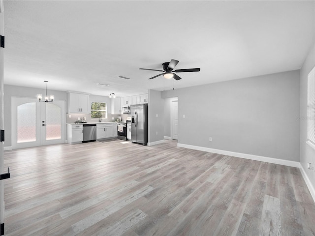 unfurnished living room with sink, french doors, ceiling fan with notable chandelier, and light wood-type flooring