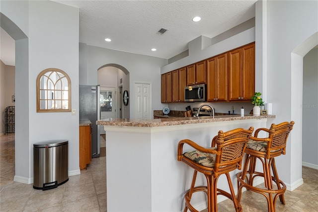 kitchen featuring sink, kitchen peninsula, a textured ceiling, a breakfast bar, and appliances with stainless steel finishes