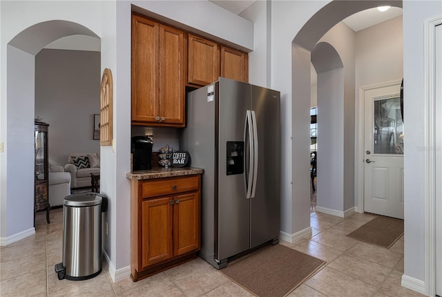 kitchen featuring light tile patterned flooring, stainless steel refrigerator with ice dispenser, and dark stone counters