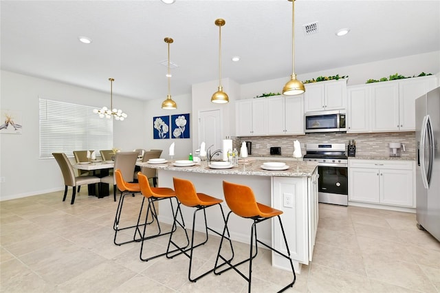 kitchen featuring light stone countertops, stainless steel appliances, decorative light fixtures, a center island with sink, and white cabinetry