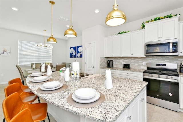 kitchen with white cabinets, pendant lighting, stainless steel appliances, and an island with sink