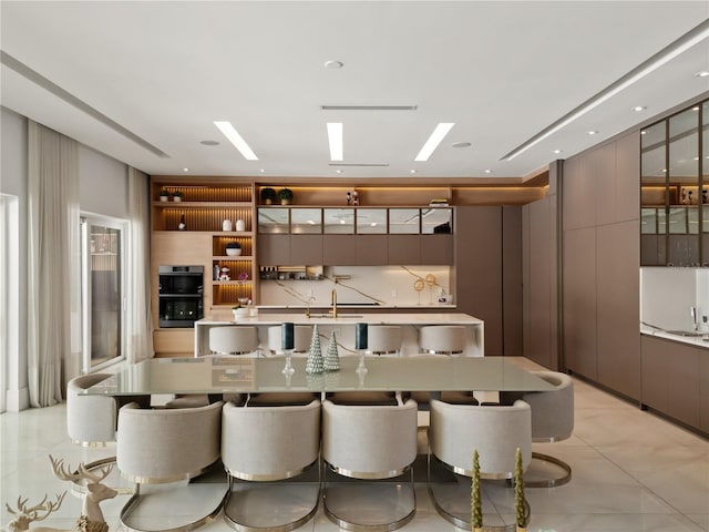 interior space featuring backsplash, stainless steel double oven, sink, light tile patterned floors, and a breakfast bar area