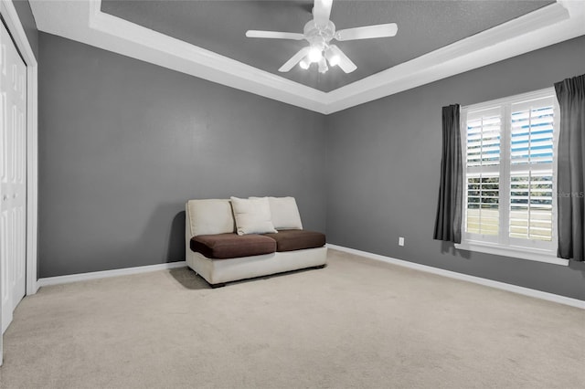 living area with light carpet, a raised ceiling, and ceiling fan