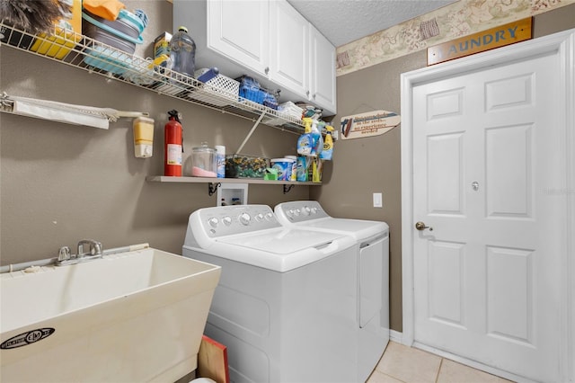 clothes washing area featuring sink, cabinets, a textured ceiling, light tile patterned flooring, and washer and dryer