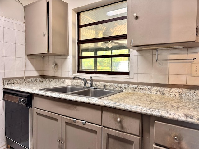 kitchen featuring light stone countertops, tasteful backsplash, gray cabinetry, sink, and black dishwasher