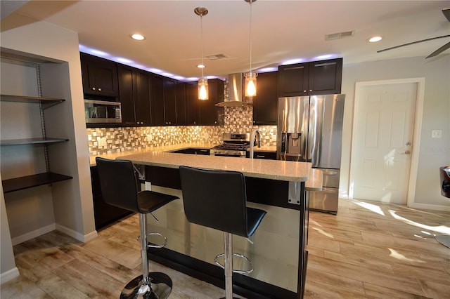 kitchen featuring pendant lighting, light hardwood / wood-style flooring, a breakfast bar area, appliances with stainless steel finishes, and wall chimney exhaust hood