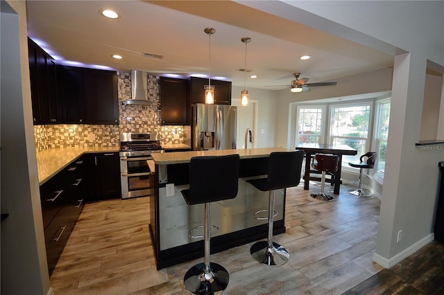 kitchen with a breakfast bar area, stainless steel appliances, a kitchen island, decorative backsplash, and wall chimney exhaust hood