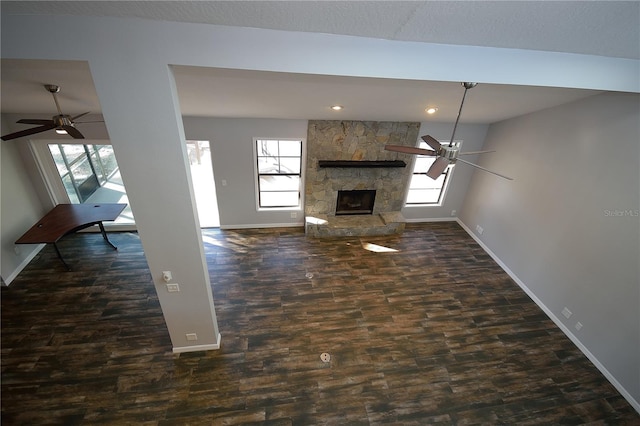 unfurnished living room with a stone fireplace, dark wood-type flooring, and ceiling fan