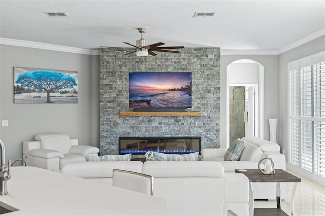 living room with a fireplace, a textured ceiling, a wealth of natural light, and crown molding