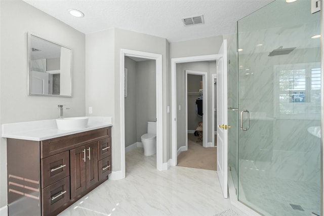 bathroom featuring a textured ceiling, vanity, toilet, and a shower with door