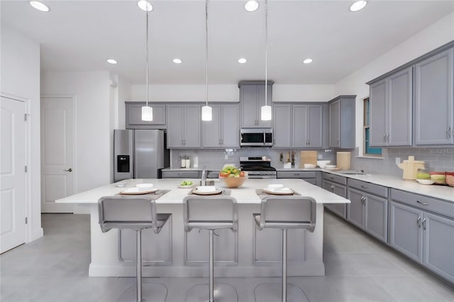 kitchen featuring gray cabinetry, a center island, decorative light fixtures, decorative backsplash, and appliances with stainless steel finishes