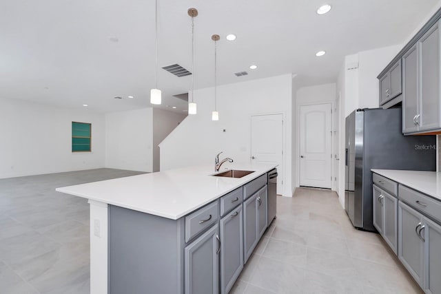 kitchen with stainless steel appliances, sink, pendant lighting, gray cabinets, and an island with sink