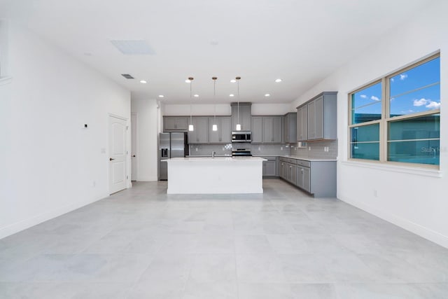 kitchen with tasteful backsplash, decorative light fixtures, gray cabinets, a center island with sink, and appliances with stainless steel finishes