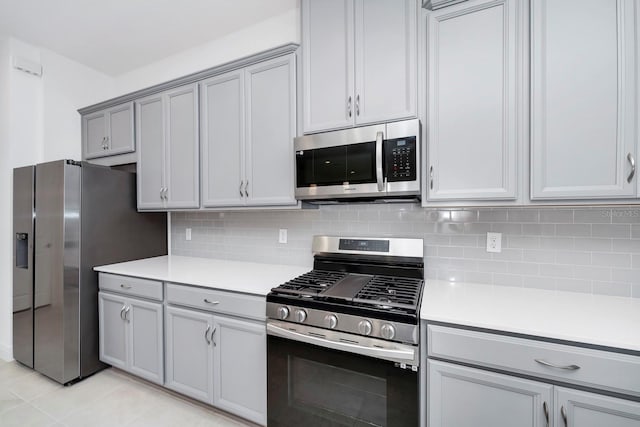 kitchen featuring appliances with stainless steel finishes, backsplash, light tile patterned floors, and gray cabinetry