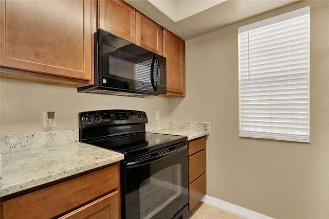 kitchen with light tile patterned floors, light stone counters, and black appliances