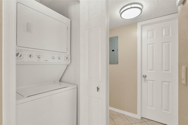 washroom with a textured ceiling, light tile patterned floors, stacked washer / dryer, and electric panel