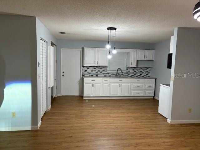 kitchen featuring tasteful backsplash, sink, decorative light fixtures, light hardwood / wood-style flooring, and white cabinets