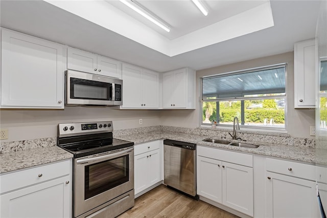 kitchen featuring appliances with stainless steel finishes, a tray ceiling, sink, white cabinets, and light hardwood / wood-style floors