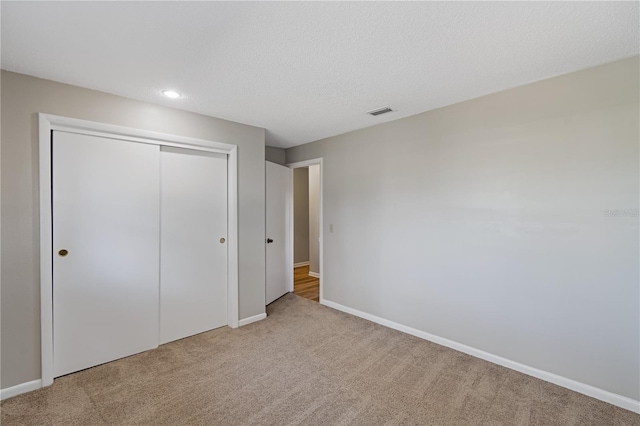 unfurnished bedroom with light carpet, a textured ceiling, and a closet