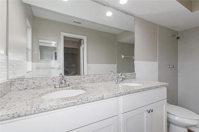 bathroom featuring tiled shower, vanity, toilet, and tile walls