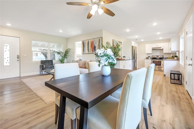 dining space featuring ceiling fan, sink, and light wood-type flooring