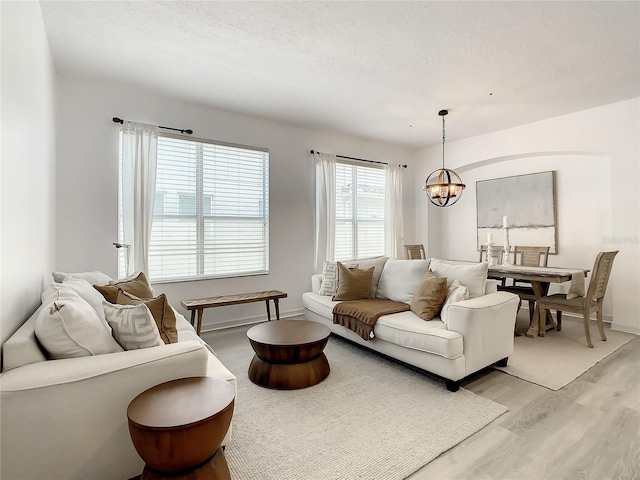 living room with light wood-type flooring, an inviting chandelier, and a textured ceiling