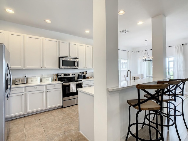 kitchen with appliances with stainless steel finishes, hanging light fixtures, white cabinets, light tile patterned floors, and a kitchen bar