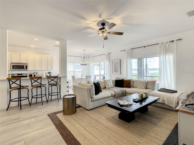 living room featuring ceiling fan with notable chandelier and light hardwood / wood-style flooring