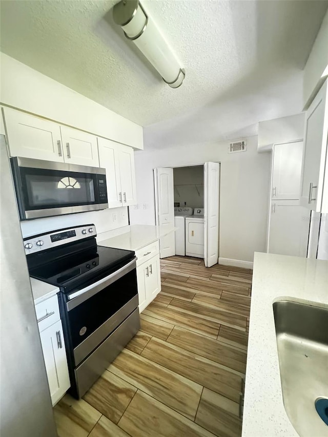 kitchen with white cabinets, sink, independent washer and dryer, a textured ceiling, and stainless steel appliances