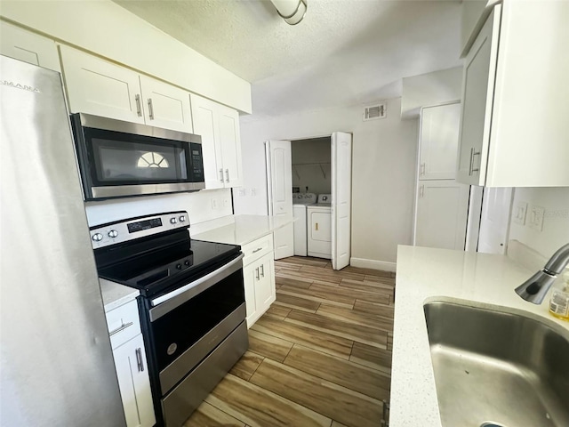 kitchen with sink, stainless steel appliances, light hardwood / wood-style floors, washer and clothes dryer, and white cabinets