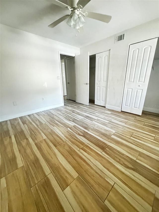 unfurnished bedroom featuring ceiling fan, light wood-type flooring, and two closets