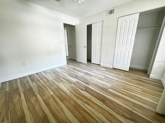 unfurnished bedroom featuring ceiling fan, light hardwood / wood-style flooring, and two closets