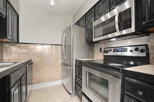 5929 Windhover Dr Unit A02, Orlando, FL 32819 - kitchen featuring appliances with stainless steel finishes, dark cabinets, light countertops, light tile patterned floors, and backsplash