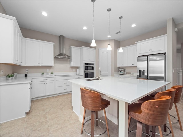 kitchen with white cabinets, wall chimney exhaust hood, stainless steel appliances, and a kitchen island with sink